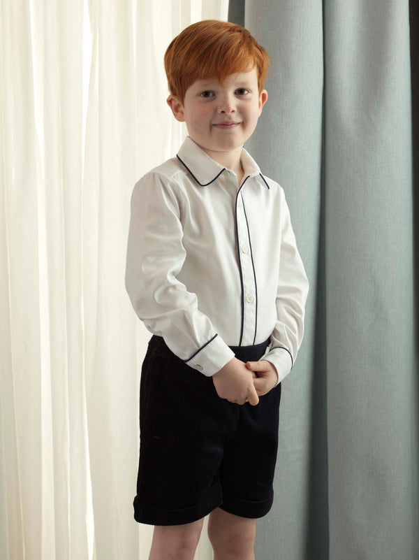 Boy wearing Navy piped pique shirt styled with navy corduroy shorts and white knee socks.